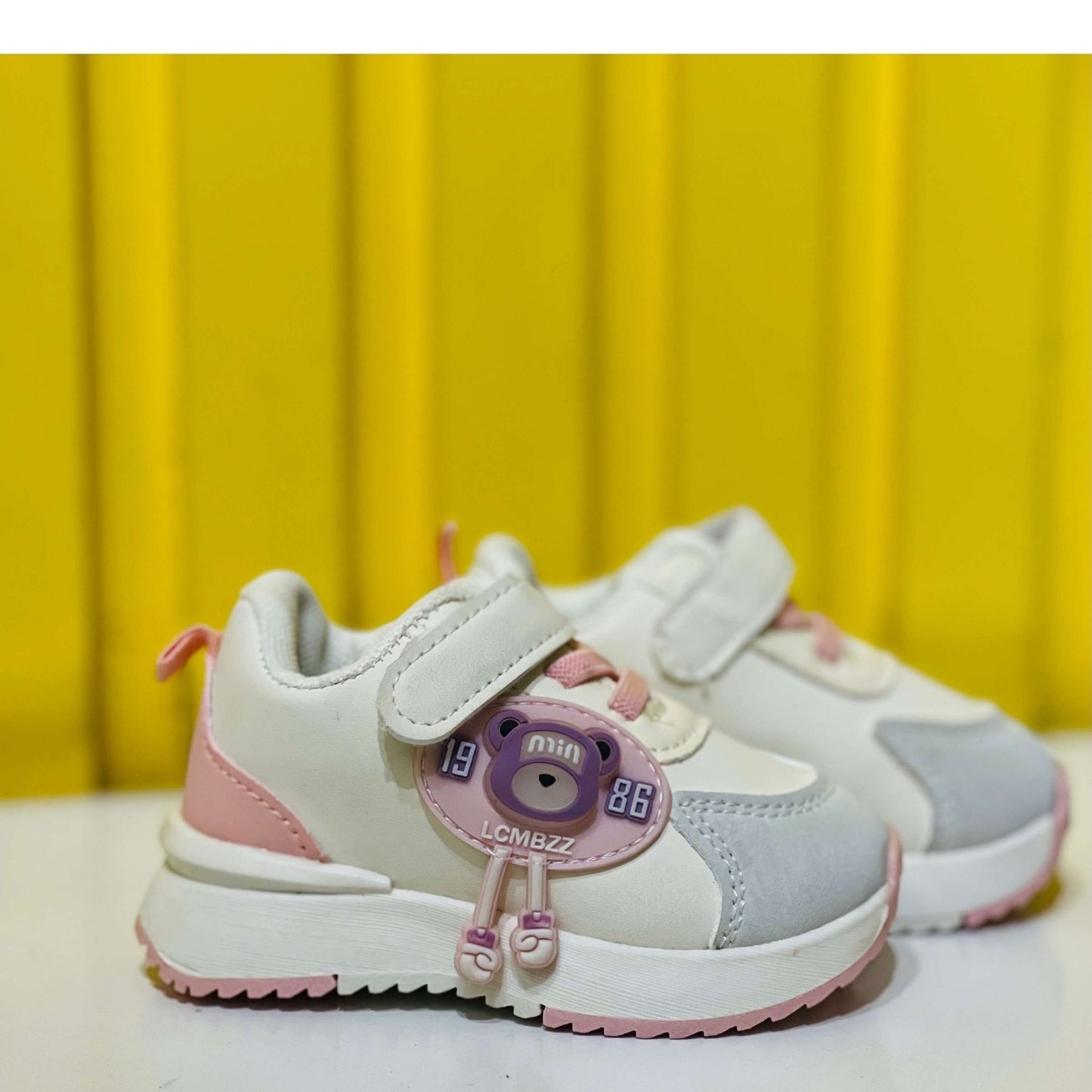 Pair of children's sneakers with pink and gray design on a yellow background