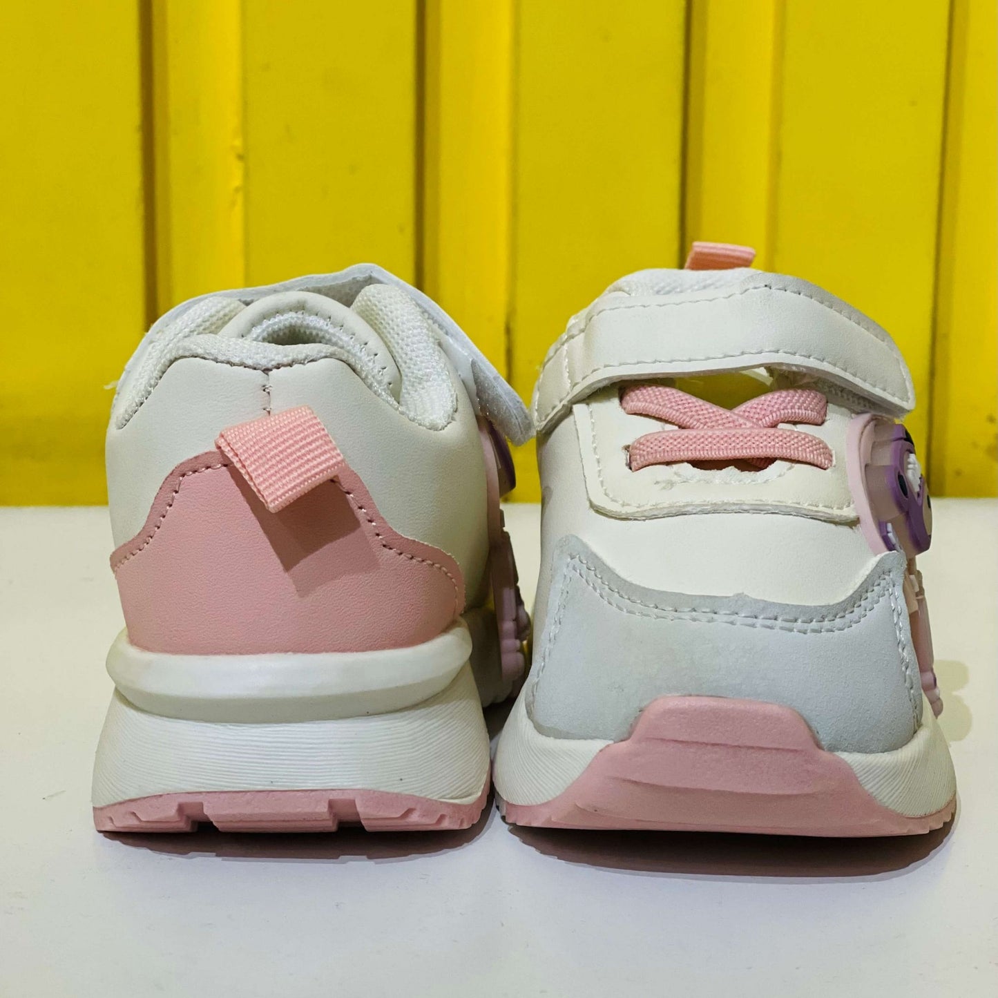 Pair of pink and white children's sneakers on a yellow background