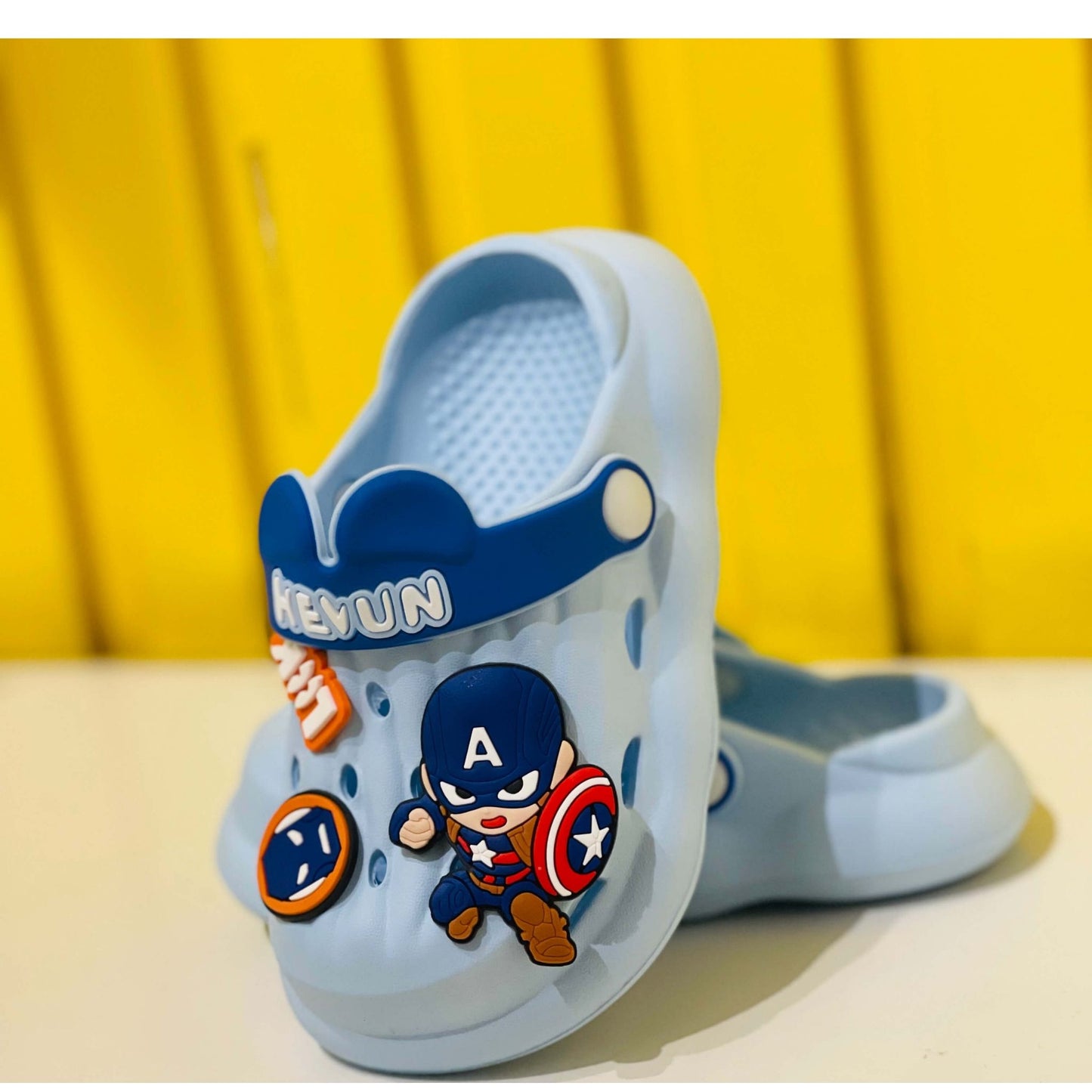 Blue children's clogs with superhero design on a yellow background