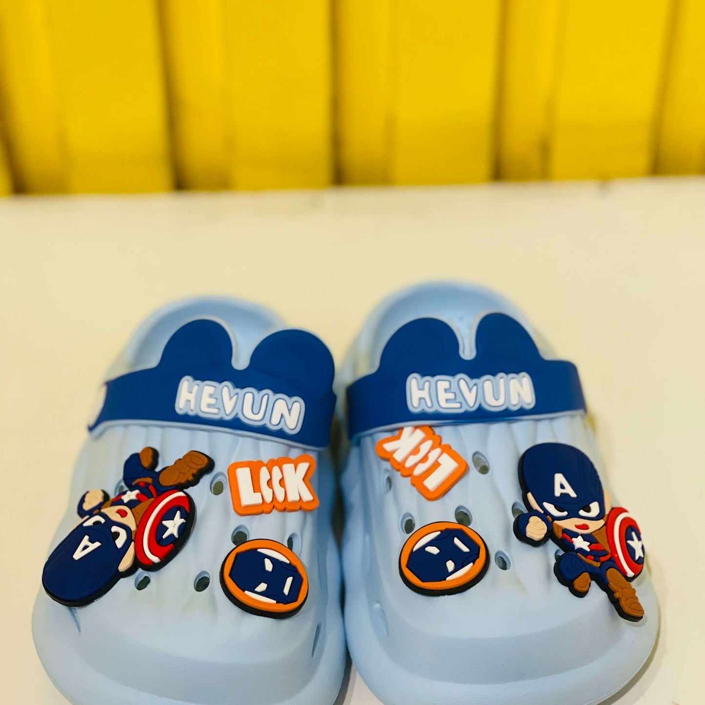 Blue children's sandals with superhero-themed decorations on a yellow background