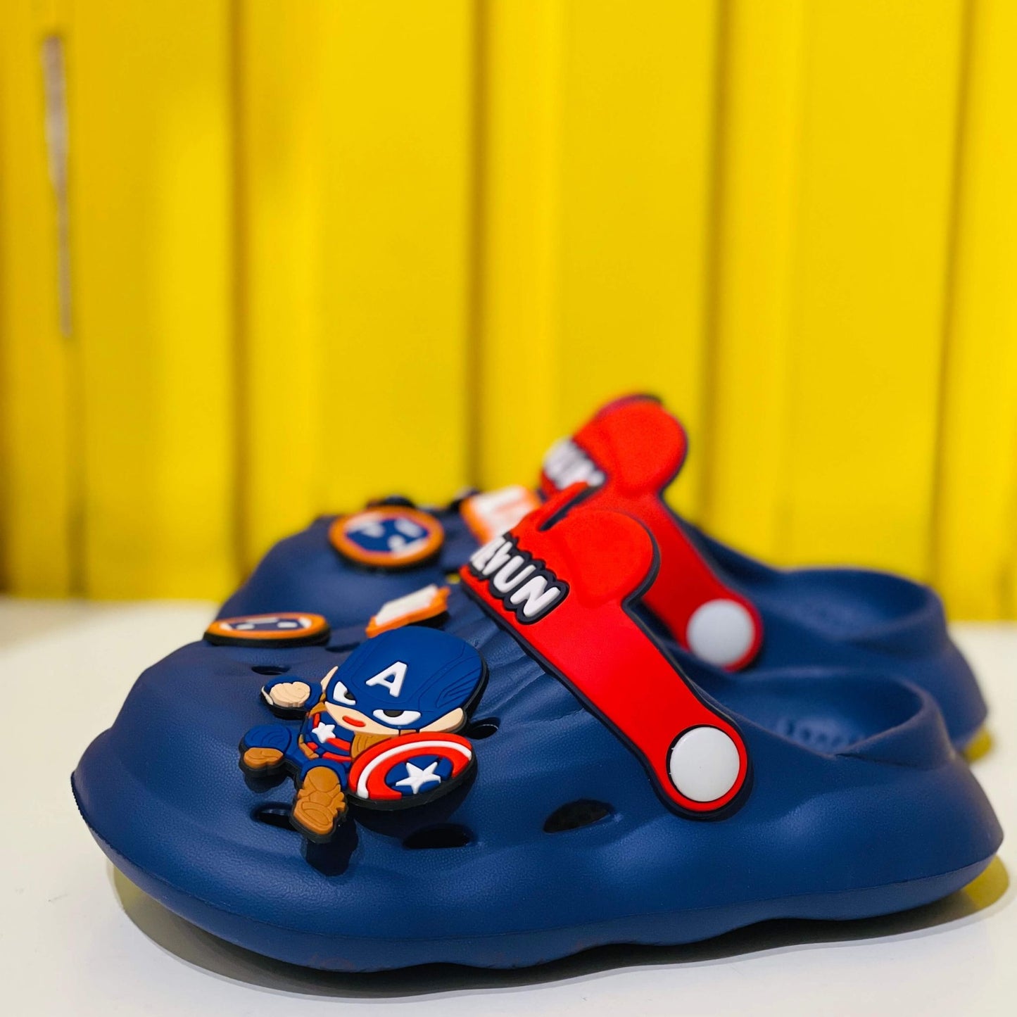 Blue children's shoes with superhero design on a yellow background