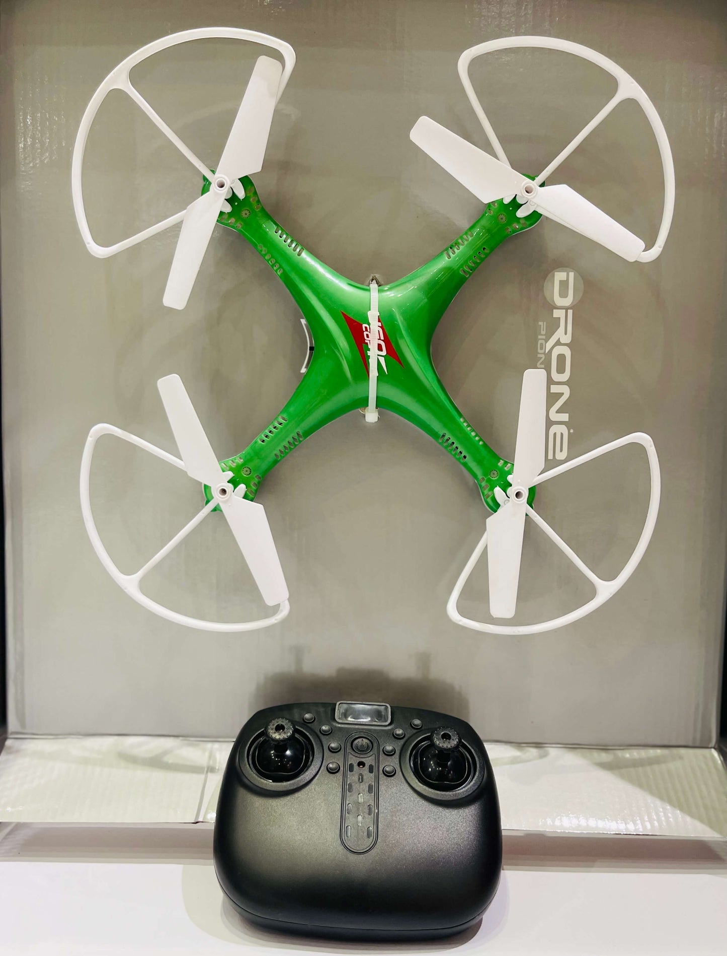 Green drone with white propellers and a black remote control on a reflective surface.