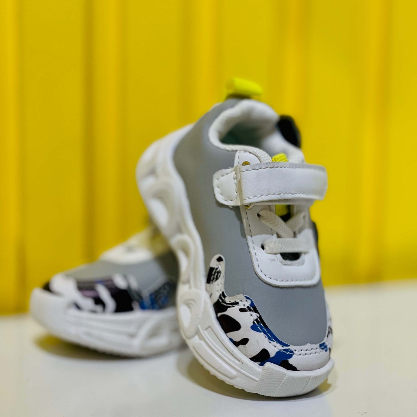 Gray and white children's shoes with cow print on a yellow background