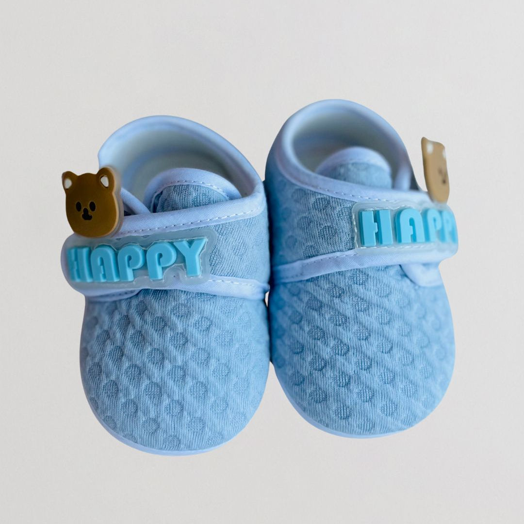 Pair of blue baby shoes with 'Happy' and bear design on a light gray background