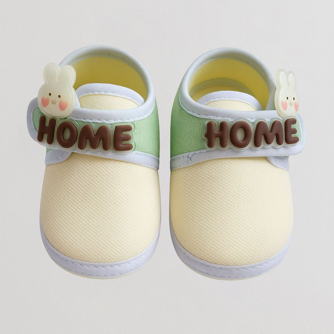 Pair of baby shoes with 'HOME' label and bunny decorations on a light gray background