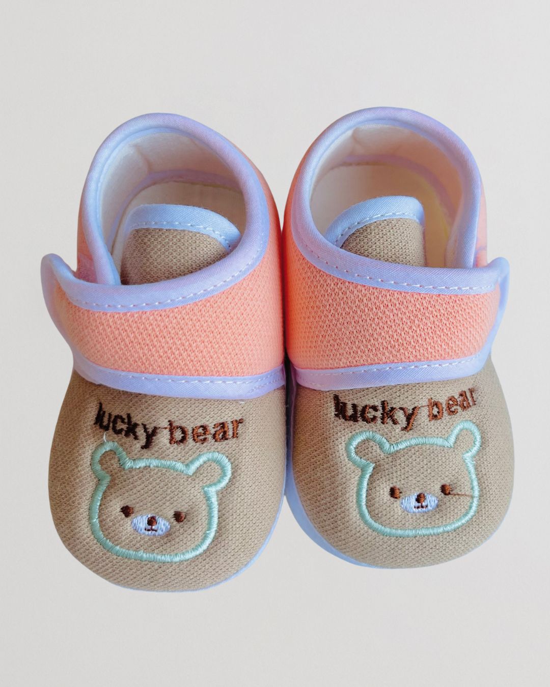 Pair of baby shoes with 'lucky bear' design on a light background