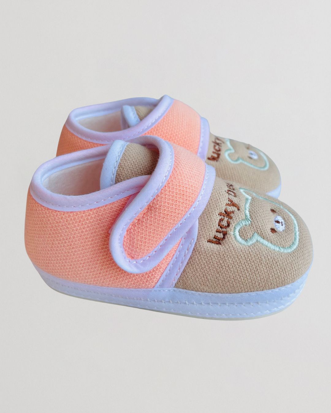 Pair of baby shoes with pink and beige design on a light background