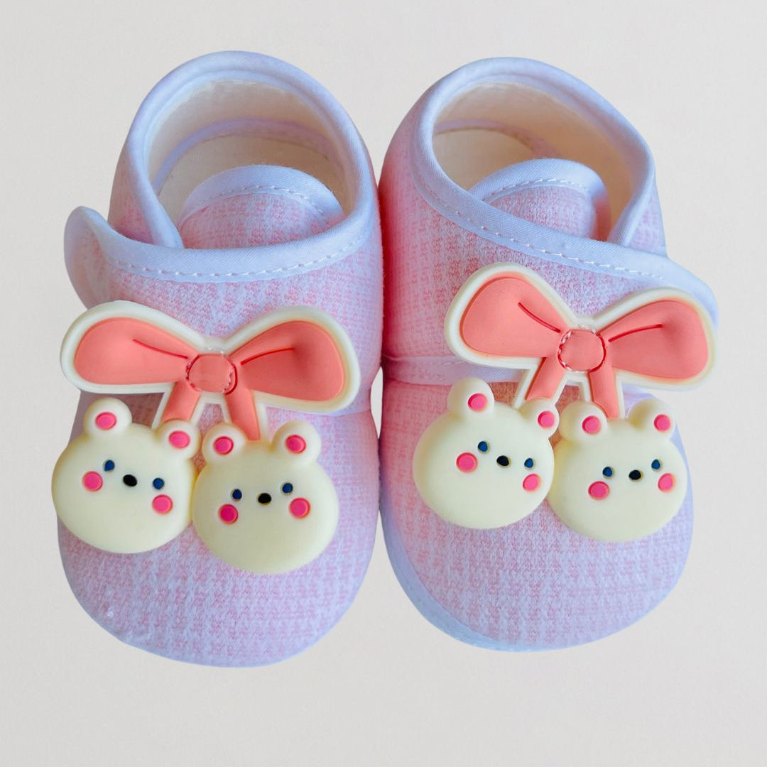 Pair of baby shoes with pink bows and bear charms on a light background