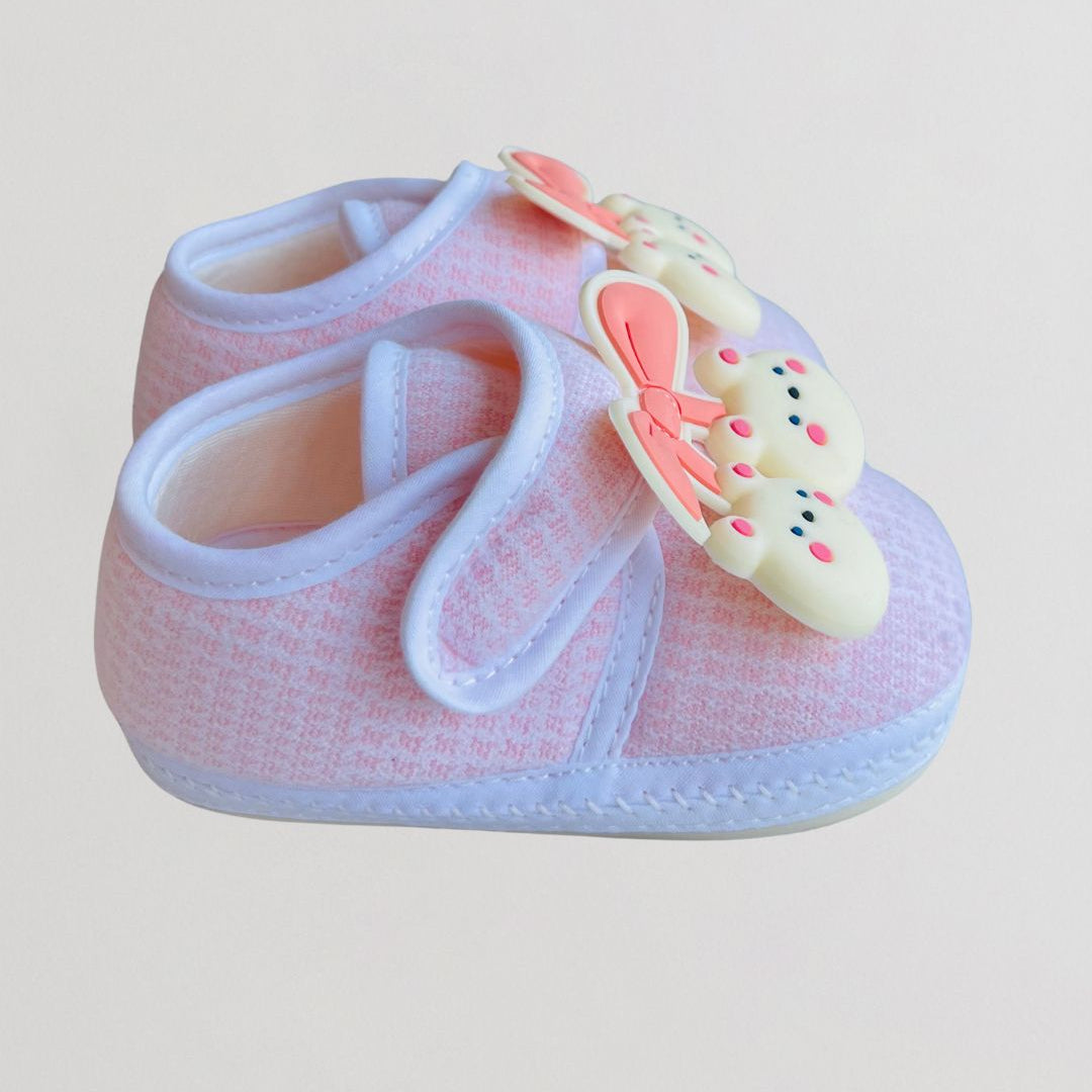 Pink baby shoe with a bow on a light gray background
