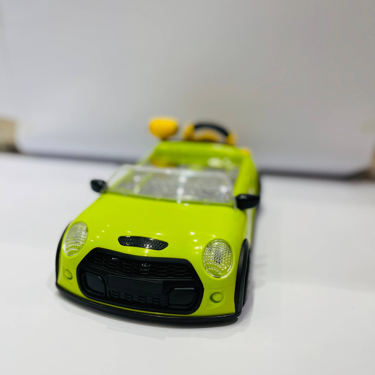 Green toy car on a white surface with a blurred background