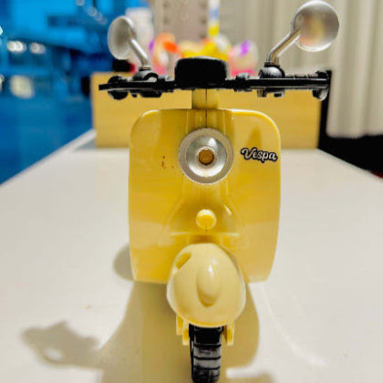 Yellow Vespa scooter model on a white surface with a blurred background