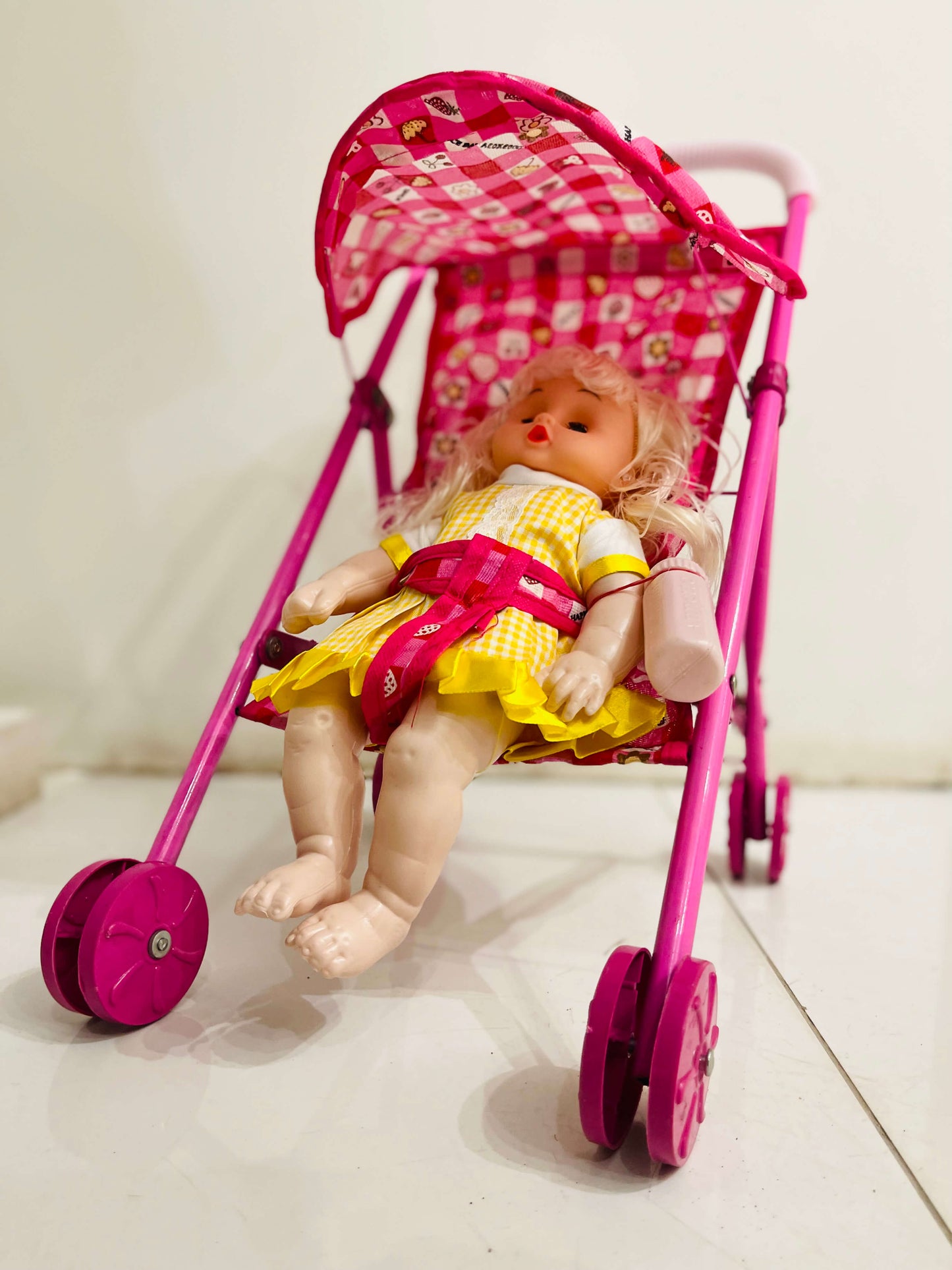 Toy doll in a pink stroller with a checkered pattern on a light background