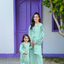 Woman and child in matching outfits standing in front of a purple door and white wall.