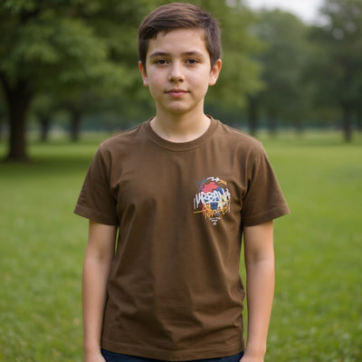 Young boy wearing a brown t-shirt with a colorful graphic in a park.