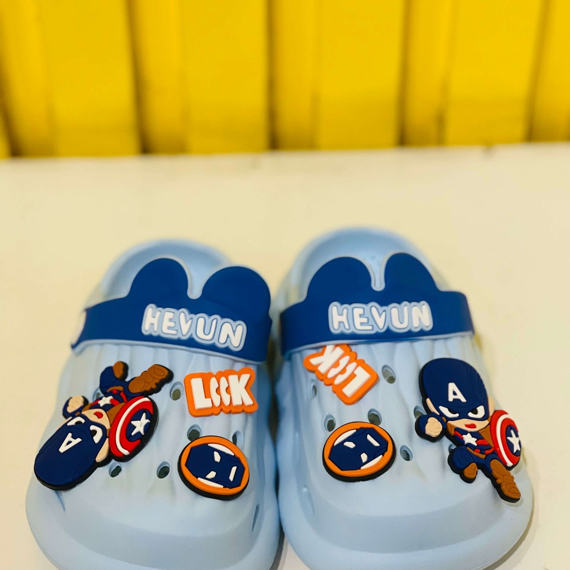 Blue children's sandals with superhero-themed decorations on a yellow background