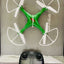 Green drone with white propellers and a black remote control on a reflective surface.