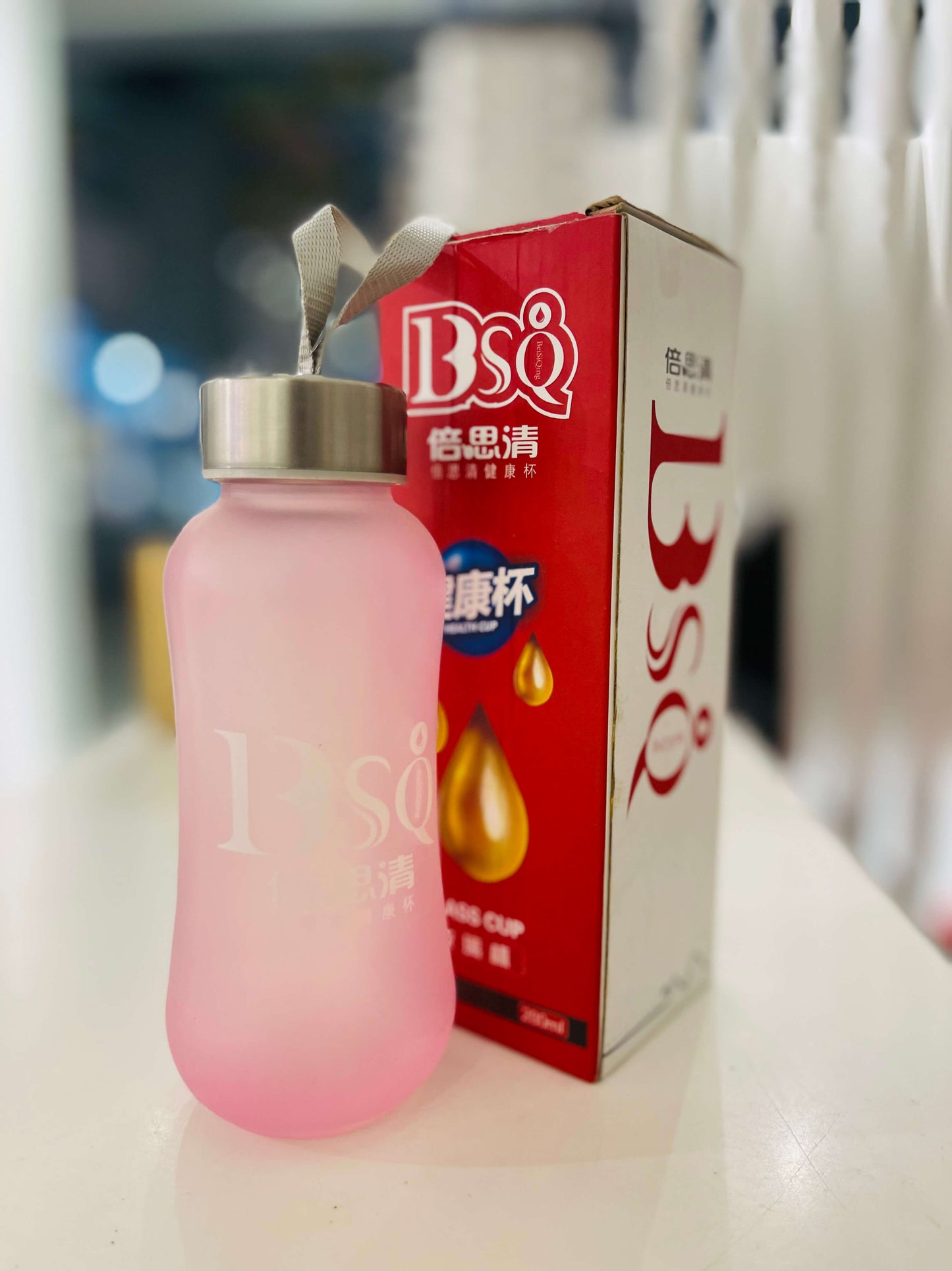 Pink tumbler with a straw next to a red box labeled 'BSQ' on a blurred background