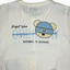 White t-shirt with a graphic of a bear wearing a blue cap and text on the back