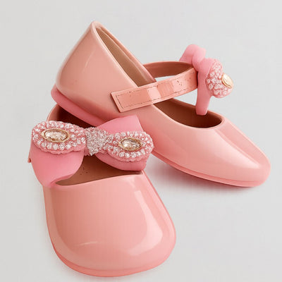 Pink children's shoes with decorative bows on a light gray background
