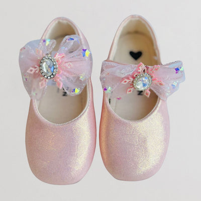Pair of pink glittery shoes with decorative bows and rhinestones on a light gray background