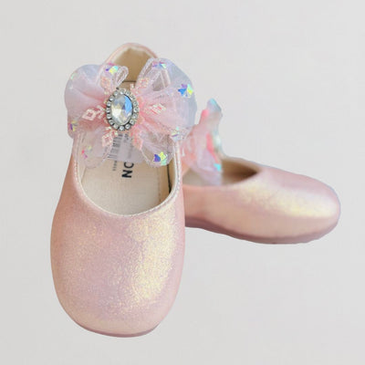 Pink glittery shoe with a decorative bow and rhinestone on a light gray background