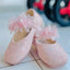 Pink children's shoes with floral designs and ribbons on a tiled floor.