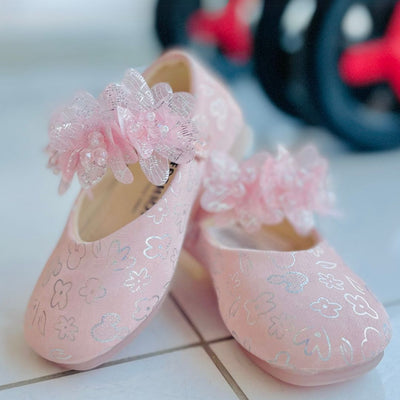 Pink children's shoes with floral designs and ribbons on a tiled floor.