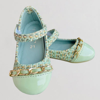 Pair of light blue shoes with gold chain details on a light gray background