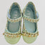 Pair of green shoes with woven design and gold chain details on a light gray background