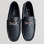 Pair of black loafers with metallic buckle on a light gray background