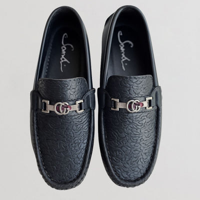 Pair of black loafers with metallic buckle on a light gray background