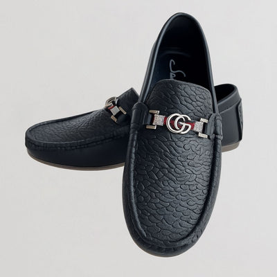 Black loafers with a silver logo on a light gray background