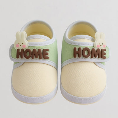 Pair of baby shoes with 'HOME' and bunny designs on a light gray background
