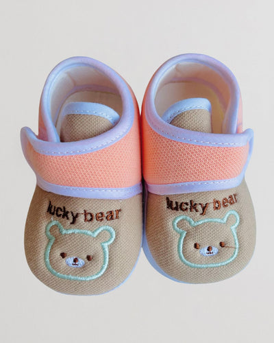 Pair of baby shoes with 'lucky bear' design on a light background