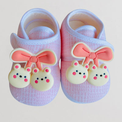 Pair of baby shoes with pink bows and bear charms on a light background