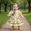 Child in a yellow dress with floral patterns standing on a path in a park.