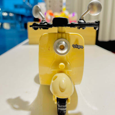 Yellow Vespa scooter model on a white surface with a blurred background