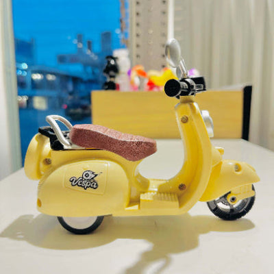 Yellow Vespa toy with a pink sponge on a white surface