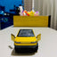 Yellow toy car on a white surface with a blurred background