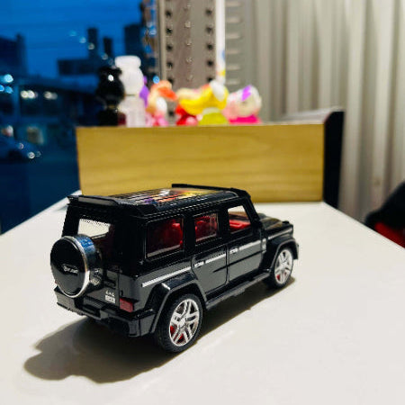 Black toy SUV on a white surface with a blurred cityscape in the background