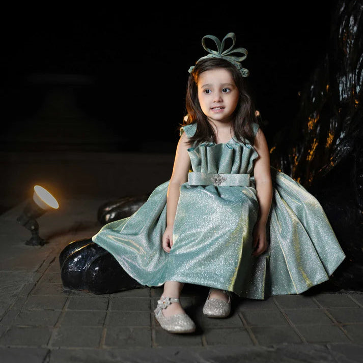 Young girl in a sparkly dress sitting on a stone surface with a dark background
