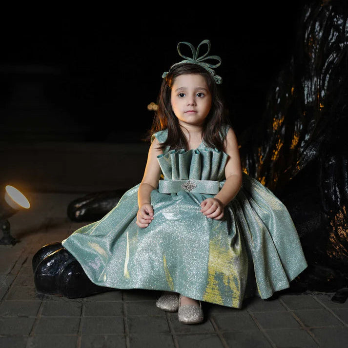 Young girl in a green dress sitting on the ground with a dark background