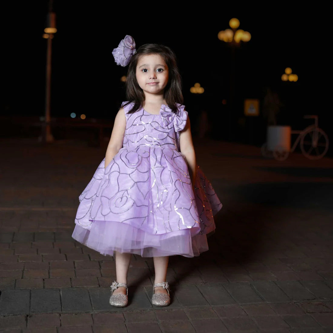 Young girl in a purple dress standing outdoors at night.