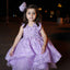 Young girl in a purple dress with a flower in her hair, standing outdoors at night.