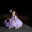 Young girl in a purple dress sitting on a stone surface at night.