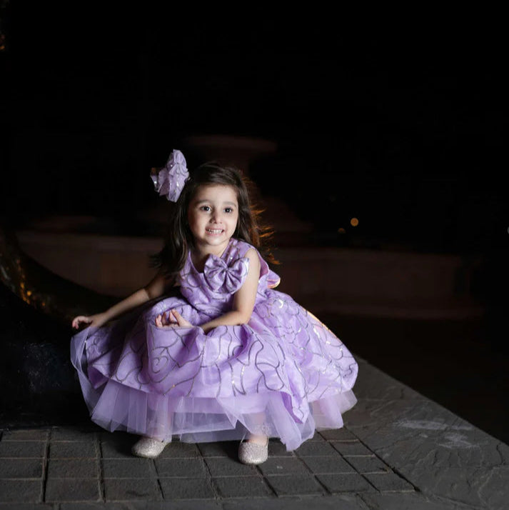 Young girl in a purple dress sitting on a stone surface at night.