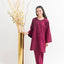 Woman in a maroon outfit standing next to a tall gold vase with decorative branches on a white background
