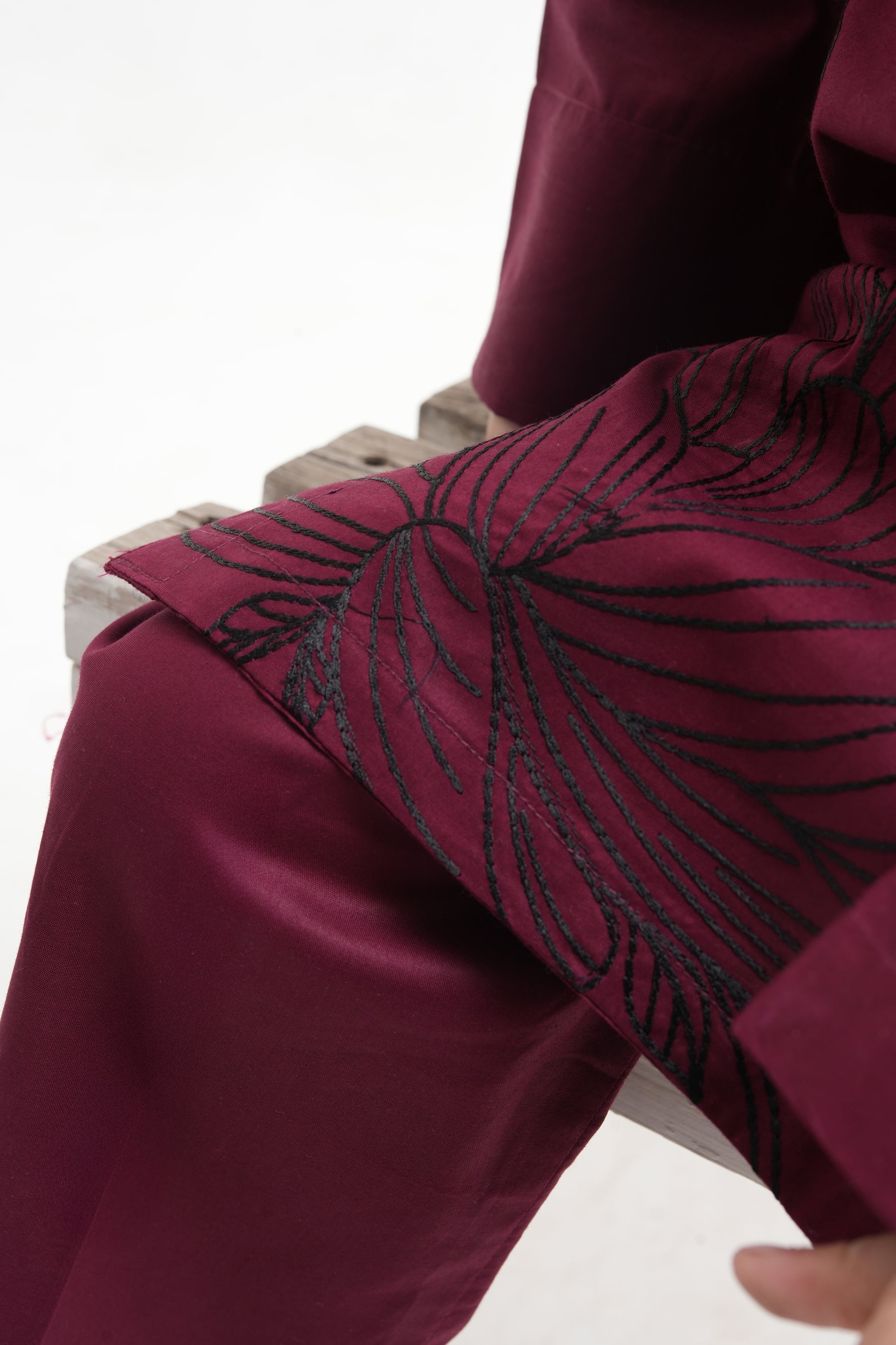 Close-up of a maroon garment with black embroidery on a white background