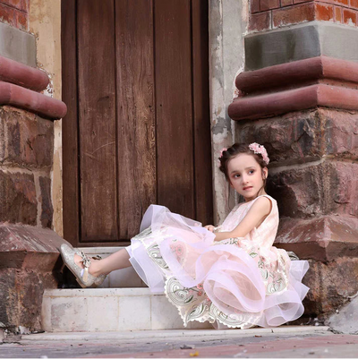 Young girl in a white dress sitting on steps in front of a brick building with a wooden door.