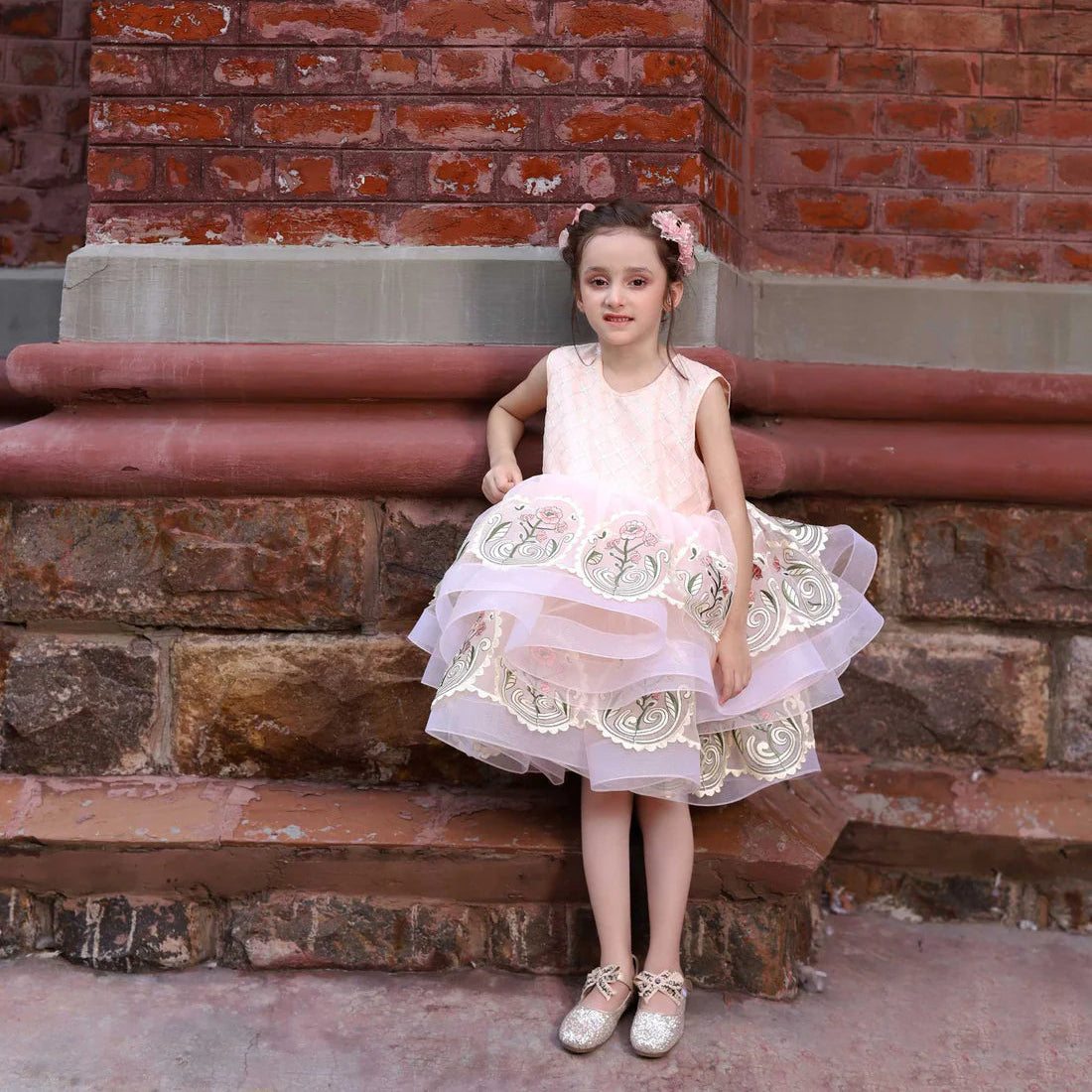 Young girl in a pink dress sitting on stone steps against a brick wall.